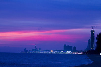 Illuminated cityscape by sea against romantic sky at sunset