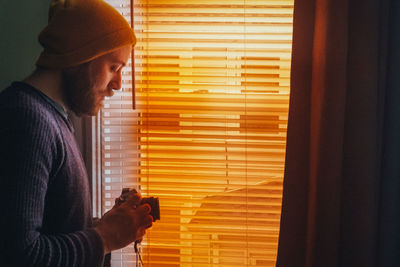 Side view of man standing against window at home