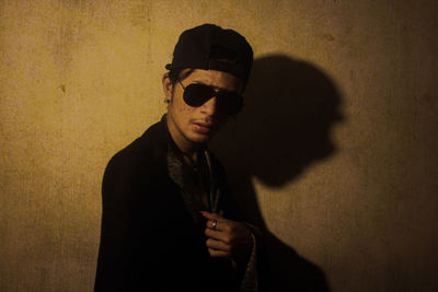 Portrait of young man wearing sunglasses standing against wall