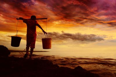 Silhouette man standing on beach against sky during sunset