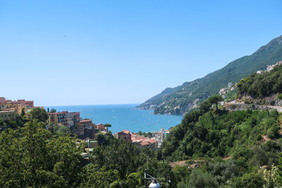 Scenic view of sea by townscape against clear blue sky