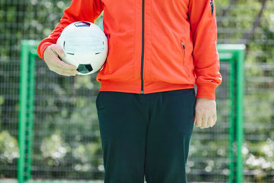 Midsection of man holding ball while standing against blurred background