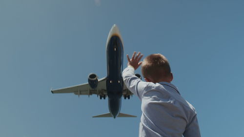 Rear view of man with airplane flying against clear blue sky