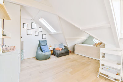 Comfortable bed with cushions and blanket placed on light mansard with pouffe in apartment