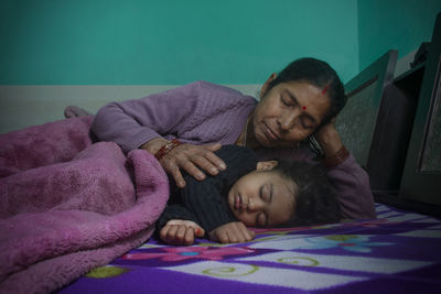 Grandmother with granddaughter sleeping on bed at home