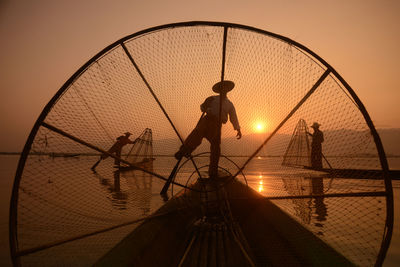 Silhouette men fishing in lake during sunset