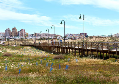 Footbridge over field in city against sky