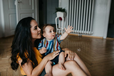 Mother playing son while sitting on floor at home