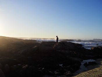 Man standing on rock by sea against clear sky