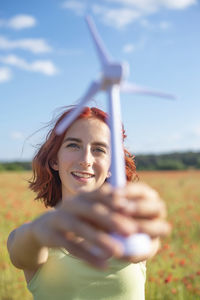 Portrait of young woman sitting on field against sky