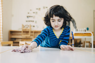 Boy cleaning table with dish cloth in child care classroom