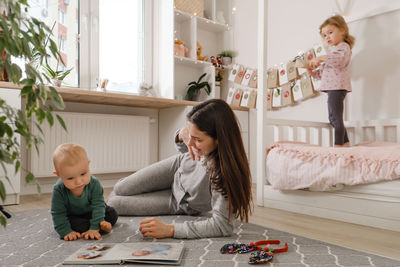 Mother spending time with two kids at home before christmas. looking photos in album, girl getting