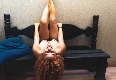 Young woman lying on bench by wall at home