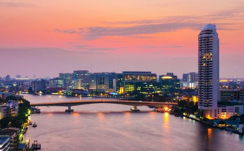 Phra pin-klao bridge over chao phraya river amidst illuminated cityscape at dusk