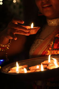 Midsection of woman holding lit diyas in plate