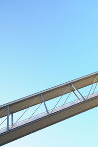 Low angle view of bridge against building against clear blue sky