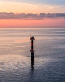Lighthouse in sea against cloudy sky at sunset