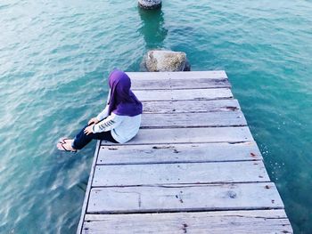 High angle view of woman sitting on pier over sea