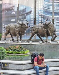 Full length of man sitting by fountain in city