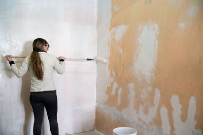 Young woman using a roller with white paint to paint the wall