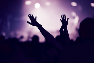 Rear view of crowd at a music concert with raising arms. stage lights in the background