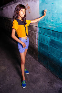 Portrait of young woman standing against wall