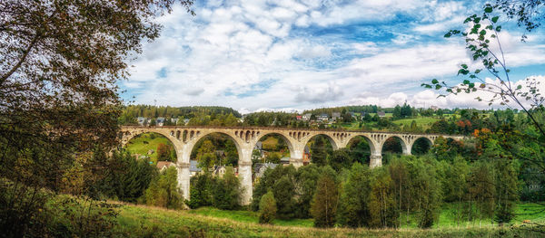 Arch bridge over trees against sky