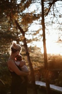 Side view of woman holding a baby standing by tree