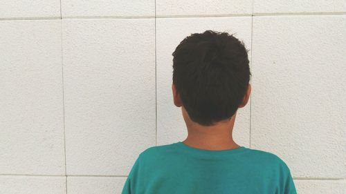 Rear view of boy standing against white wall
