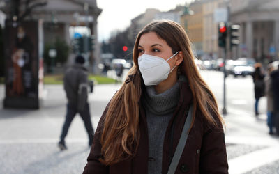 Young woman wearing mask looking away while standing outdoors