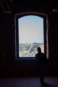 Rear view of woman looking through window