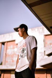 Young man looking away while standing against built structure