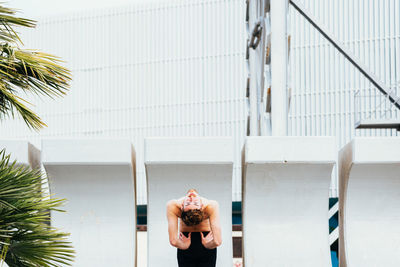 Rear view of man stretching while standing against building