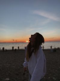 Woman standing on beach against sky during sunset