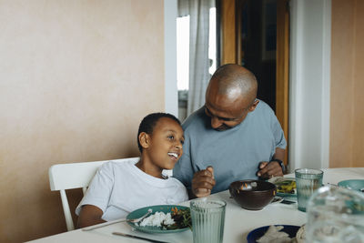 Father talking to son while sitting at dining table during lunch at home