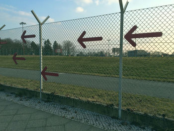 Arrow symbols on fence by road against sky