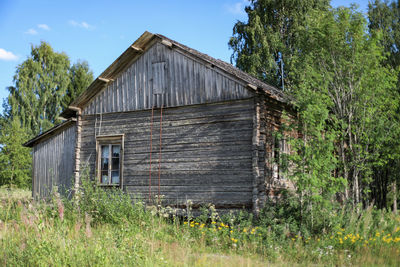 Wooden house on field by trees against sky