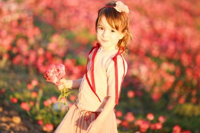 Portrait of cute smiling girl smelling pink flowers while standing on land