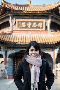 Portrait of smiling young woman standing against building
