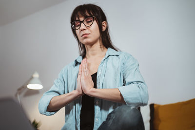 Young woman looking away while standing against wall