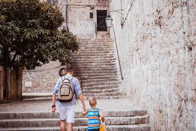 Back view of father and son walking through old town and holding hands.