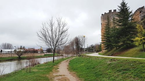 Canal amidst bare trees and buildings against sky