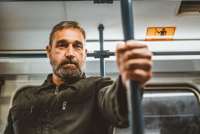 Middle-aged caucasian man driving in the city bus while standing and holding grip.