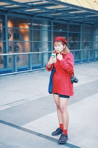 Full length of young woman using phone while standing on road