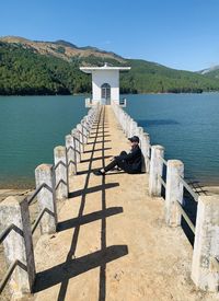 Side view of man sitting on pier by lake