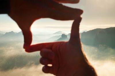 Close up of hands making frame gesture. blue misty valley. sunny spring daybreak in mountains.