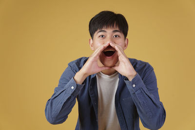 Portrait of young man standing against yellow background