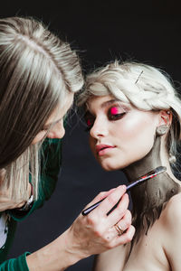 Close-up of artist applying make-up of woman against black background