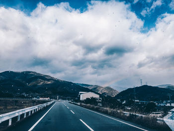 Road leading towards mountains against cloudy sky