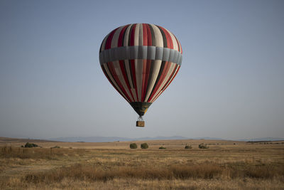 Hot air balloon flying over field against clear sky